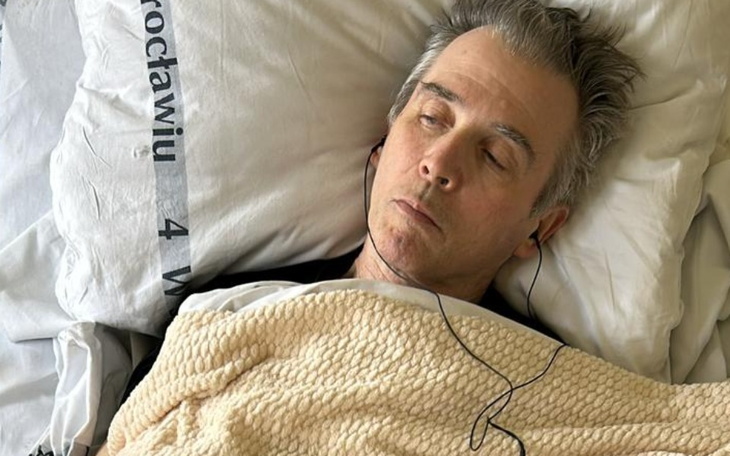 Mężczyzna leżący w łóżku, z zamkniętymi oczami, słuchawki na uszach.