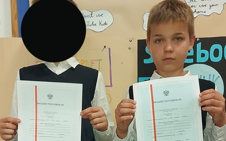 Dzieci trzymające świadectwa szkolne, z zamazanymi twarzami.