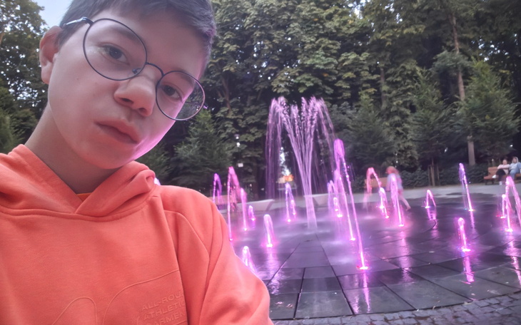 Młody chłopak z okularami, selfie przy fontannie.