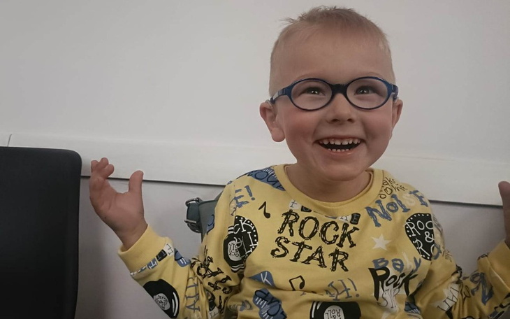 Uśmiechnięty chłopiec w okularach, ubrany w kolorową bluzę.