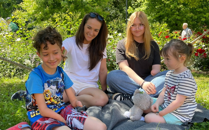 Cztery dzieci bawiące się na kocu w parku, w otoczeniu zieleni.