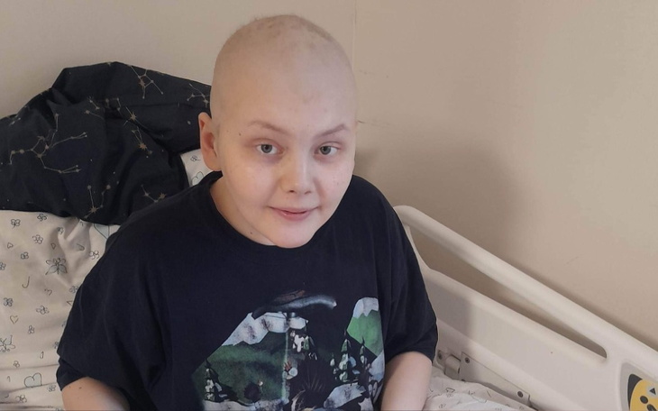 Chłopiec z łysą głową, uśmiechający się w szpitalnym łóżku.