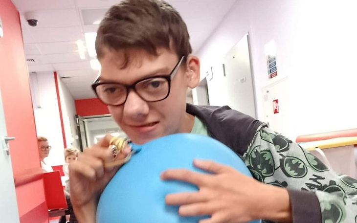 Chłopak trzyma niebieski balon, uśmiechając się w korytarzu.