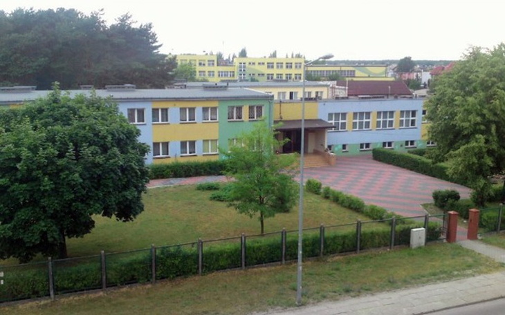 Widok na szkołę z zielonymi drzewami wokół.