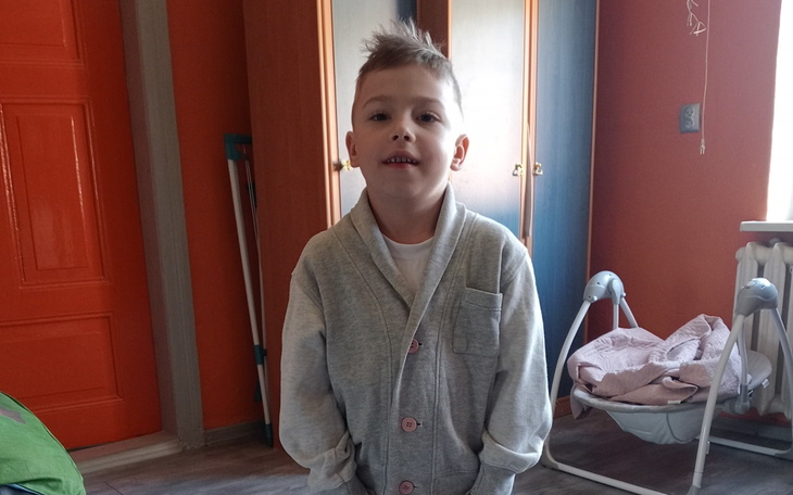 Chłopiec w szarym swetrze uśmiecha się w kolorowym pokoju.
