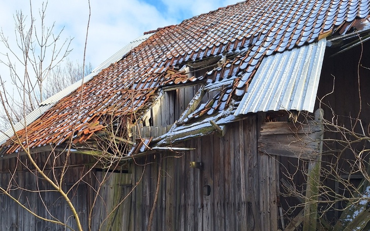 Zniszczony dach starego budynku pokryty śniegiem.