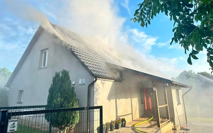 Szare budynki, teren pożarniczy z gaśnicą w dole kadru.