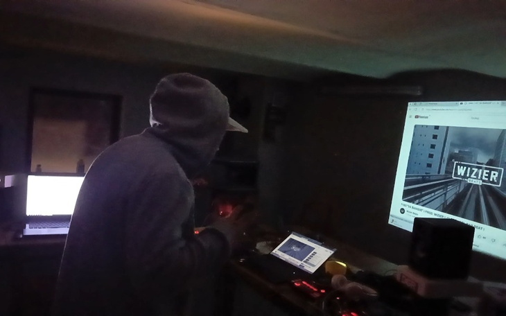 Mężczyzna w szarej bluzie pracujący przy komputerze w ciemnym pomieszczeniu.