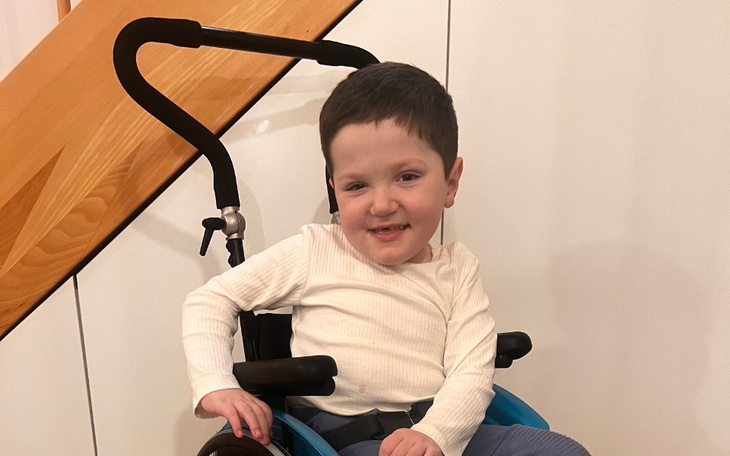 Chłopiec w wózku inwalidzkim, uśmiechający się do kamery.