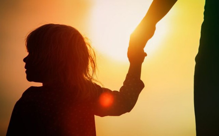 Dziecko trzymające dłoń dorosłego na tle zachodzącego słońca.