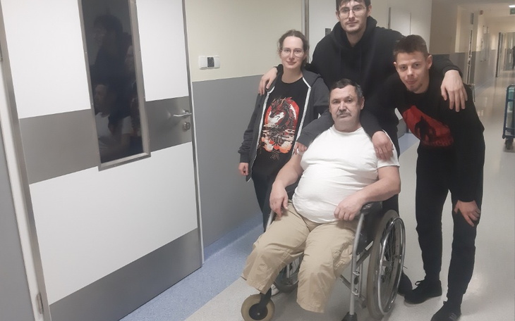 Rodzina pozująca z mężczyzną na wózku inwalidzkim w szpitalu.