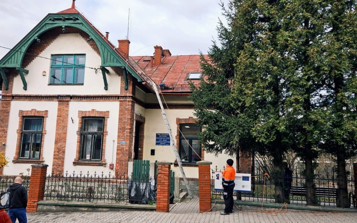 Budynek z czerwonym dachem, robotnik na drabinie, prace remontowe.