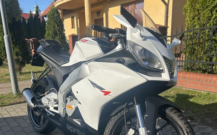 Motocykl marki Aprilia zaparkowany przed domem, w dobrym stanie.