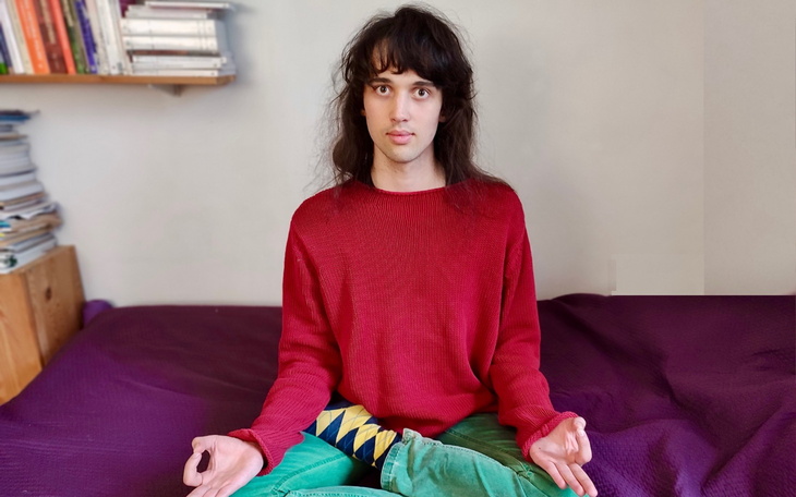 Osoba medytująca w czerwonym swetrze na fioletowej kanapie.