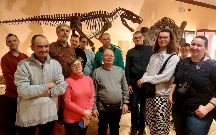 Grupa ludzi w muzeum, obok szkieletu dinozaura.