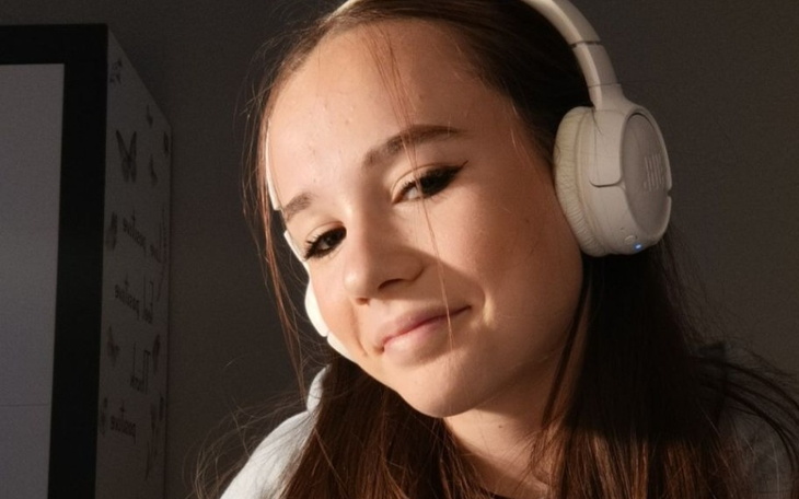 Młoda dziewczyna w słuchawkach, uśmiechająca się do kamery.