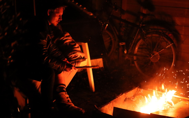 Osoba przy ognisku, w tle rower, nocna atmosfera.