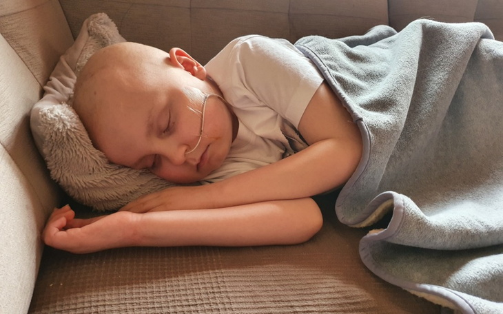 Chłopiec z chorobą nowotworową śpi na kanapie, przykryty kocem.