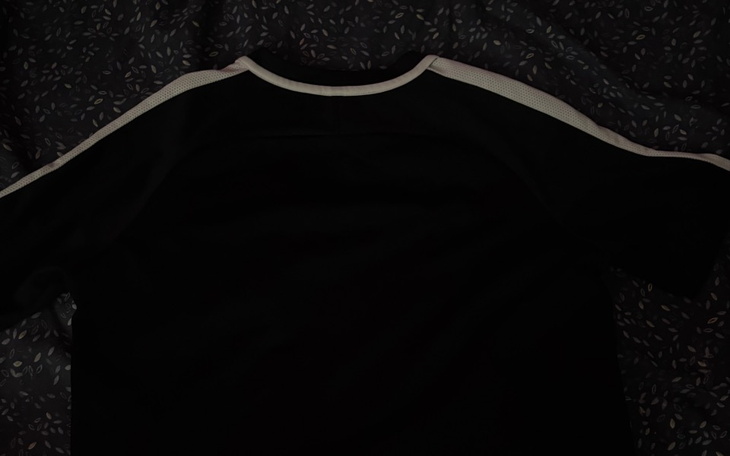 Czarny t-shirt leżący na ciemnym tle, widok z góry.