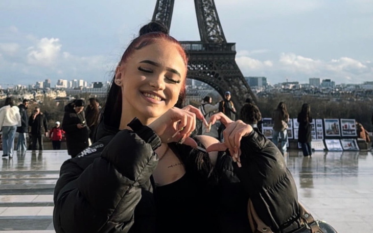 Młoda kobieta robi serce rękami przed Wieżą Eiffla.