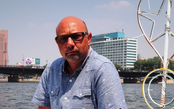 Mężczyzna w okularach, siedzący nad rzeką.