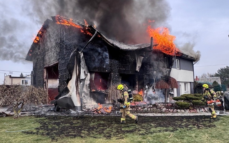Dom w płomieniach, strażacy gaszący pożar.