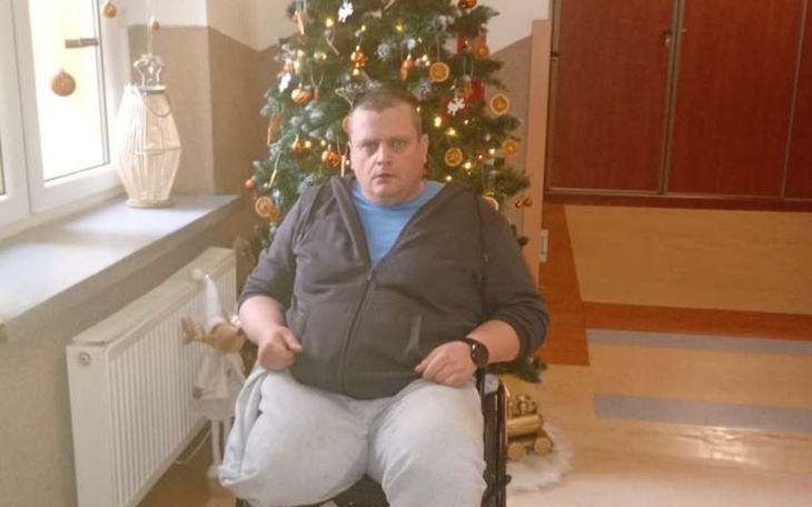 Mężczyzna na wózku inwalidzkim obok choinki w świątecznym otoczeniu.