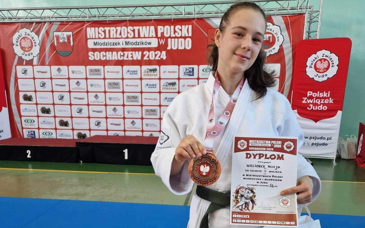 Młoda judoczka z medalem na zawodach, dumnie trzyma dyplom.