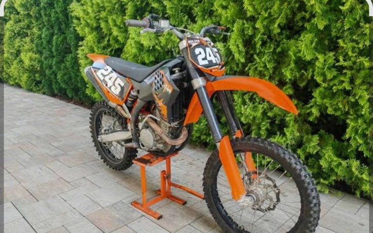 Motocykl terenowy, pomarańczowy, na stojaku.