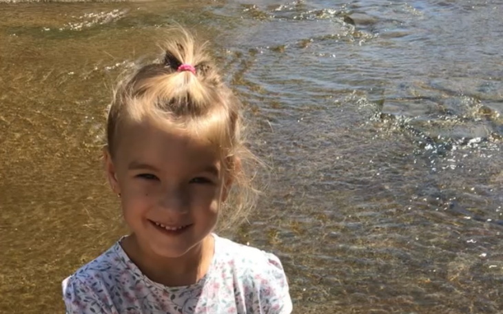 Uśmiechnięta dziewczynka przy wodzie, cieszy się chwilą spędzoną na świeżym powietrzu.