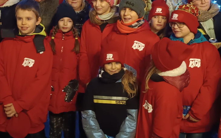 Grupa dzieci w czerwonych kurtkach, uśmiechających się do kamery.