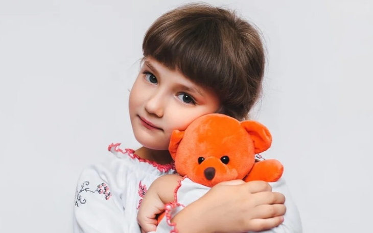 Dziewczynka przytula pluszowego misia w kolorze pomarańczowym.
