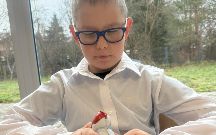 Chłopiec w białej koszuli, skupiony na rozpakowywaniu zabawki.