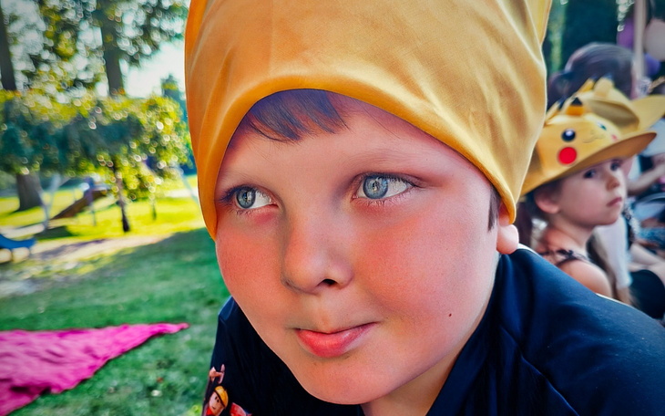 Chłopiec w żółtej chustce, z błyszczącymi oczami, na tle letniego krajobrazu.