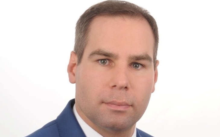 Mężczyzna w garniturze, patrzący w kamerę, na jasnym tle.