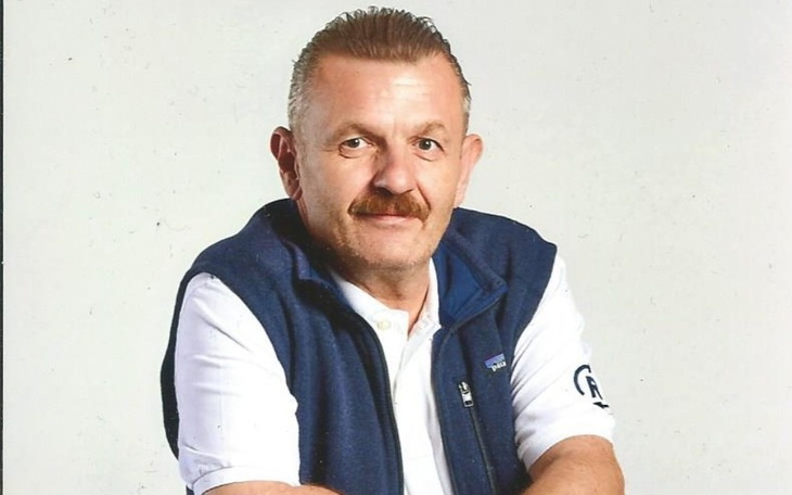 Mężczyzna w kamizelce, pozujący do zdjęcia z uśmiechem.