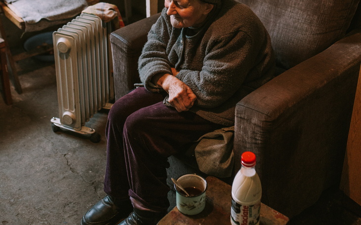 Starsza kobieta siedząca na kanapie z kubkiem herbaty.