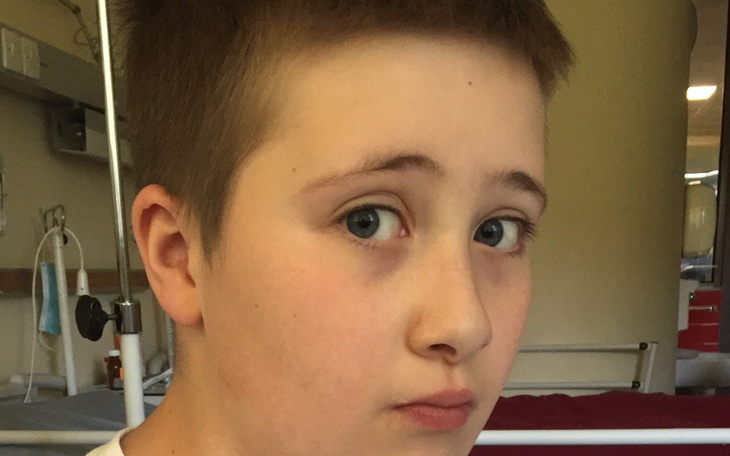 Chłopiec w szpitalu, zmartwiony, patrzy w obiektyw.