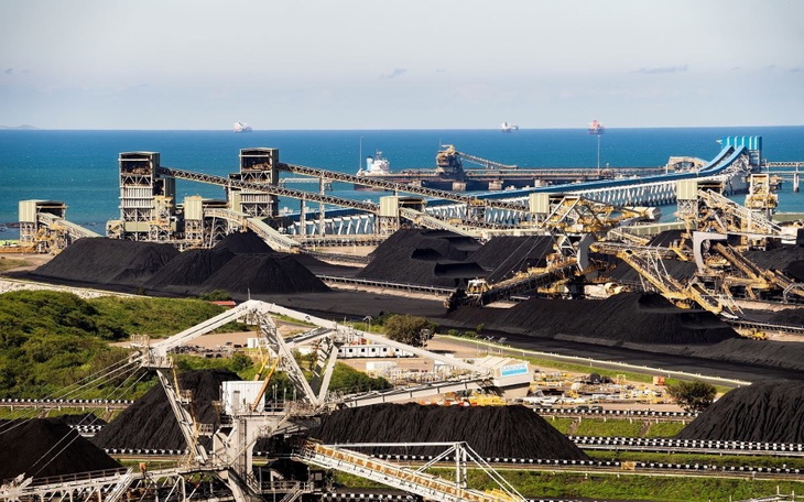 Widok na przemysłowy port z węglem i statkami na tle morza.