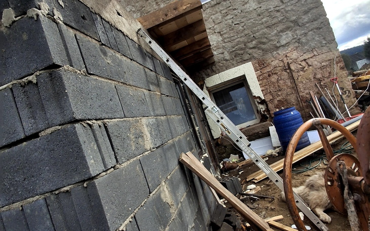 Zniszczona ściana budynku z materiałami budowlanymi w tle.