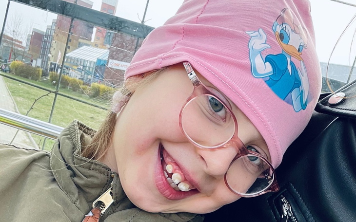 Uśmiechnięta dziewczynka w różowej czapce z postacią z bajki.
