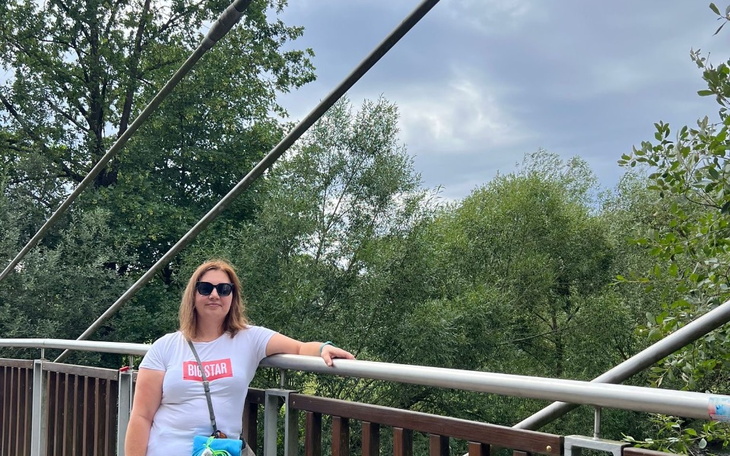 Kobieta w okularach przeciwsłonecznych, stojąca na moście wśród zieleni.