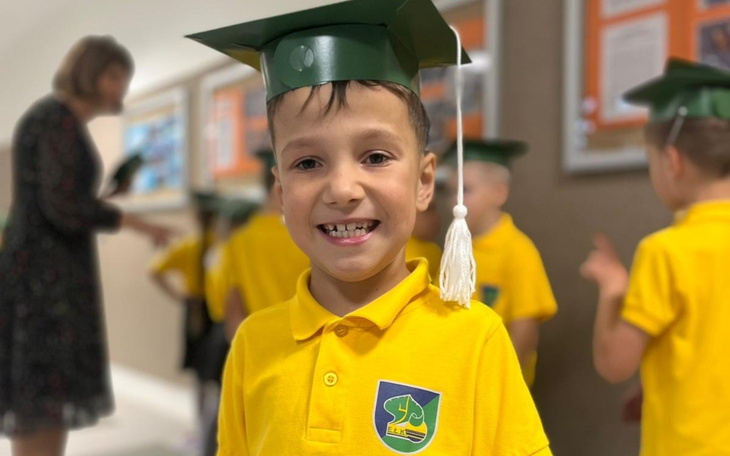 Uśmiechnięty chłopiec w żółtej koszulce i czapce absolwenta.