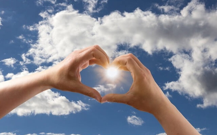 Dwie ręce tworzące serce na tle nieba z chmurami.