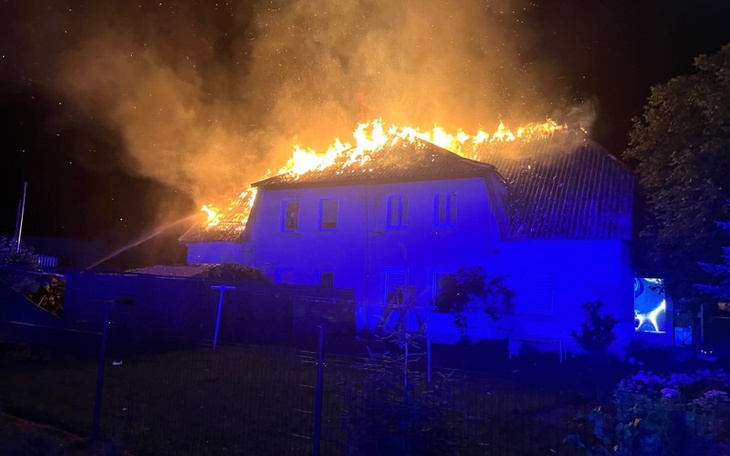 Dom w płomieniach, strażacy walczą z pożarem w nocy.