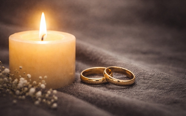 Złote obrączki ślubne obok świecy, symbol miłości i jedności.