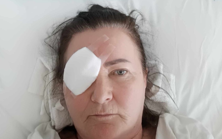 Kobieta po operacji, z opatrunkiem na oku, leżąca w łóżku.