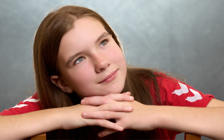 Młoda dziewczyna z zamyślonym wyrazem twarzy, opierająca się na rękach.