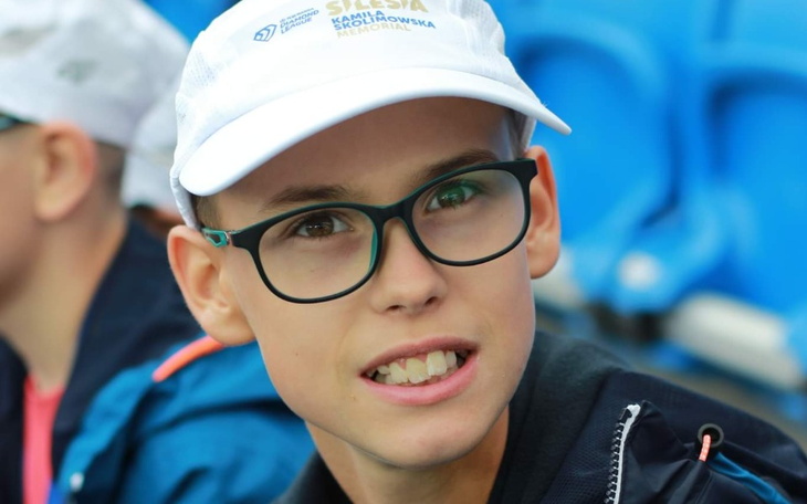 Chłopiec w czapce, uśmiechający się na tle trybun.