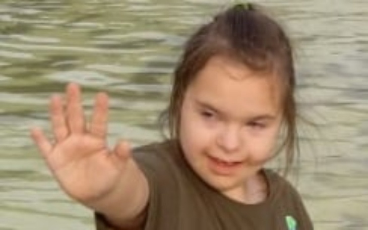 Mała dziewczynka machająca ręką w wodzie, uśmiechnięta.